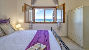 A bedroom with a bed, a window with curtains, a bedside lamp, and a view of the sea.