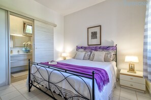 Ein Schlafzimmer mit einem Bett, Nachttischen, einem Fenster mit Jalousien und einem gerahmten Bild an der Wand.