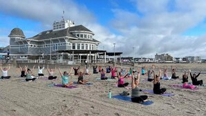 A group of people on a beach performing yoga, with a large building in the background. - Newly Renovated, all new beds and bedroom furniture (Hampton)