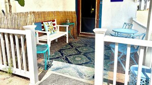 A covered outdoor seating area with a bench, chairs, and a table, a door leading inside, and a welcome sign. - Newly Renovated, all new beds and bedroom furniture (Hampton)