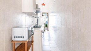 Una cocina estrecha con armarios blancos, un microondas sobre una repisa de madera y una lámpara colgante roja.