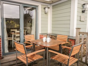 A wooden table with four chairs, a brick wall, and a glass door leading to an indoor area. - 1 Court Cottage, Hillfield Village (Dartmouth)