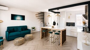 Un espacio habitable moderno con un sofá color turquesa, una mesa de comedor de madera y taburetes altos, y un patrón de suelo tipo espiga.