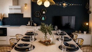 Un comedor moderno con una larga mesa dispuesta para seis comensales, sillas doradas y un jarrón central con follaje.