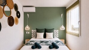 Un dormitorio con cama, dos mesitas de noche, aire acondicionado de pared y ventana con cortinas.