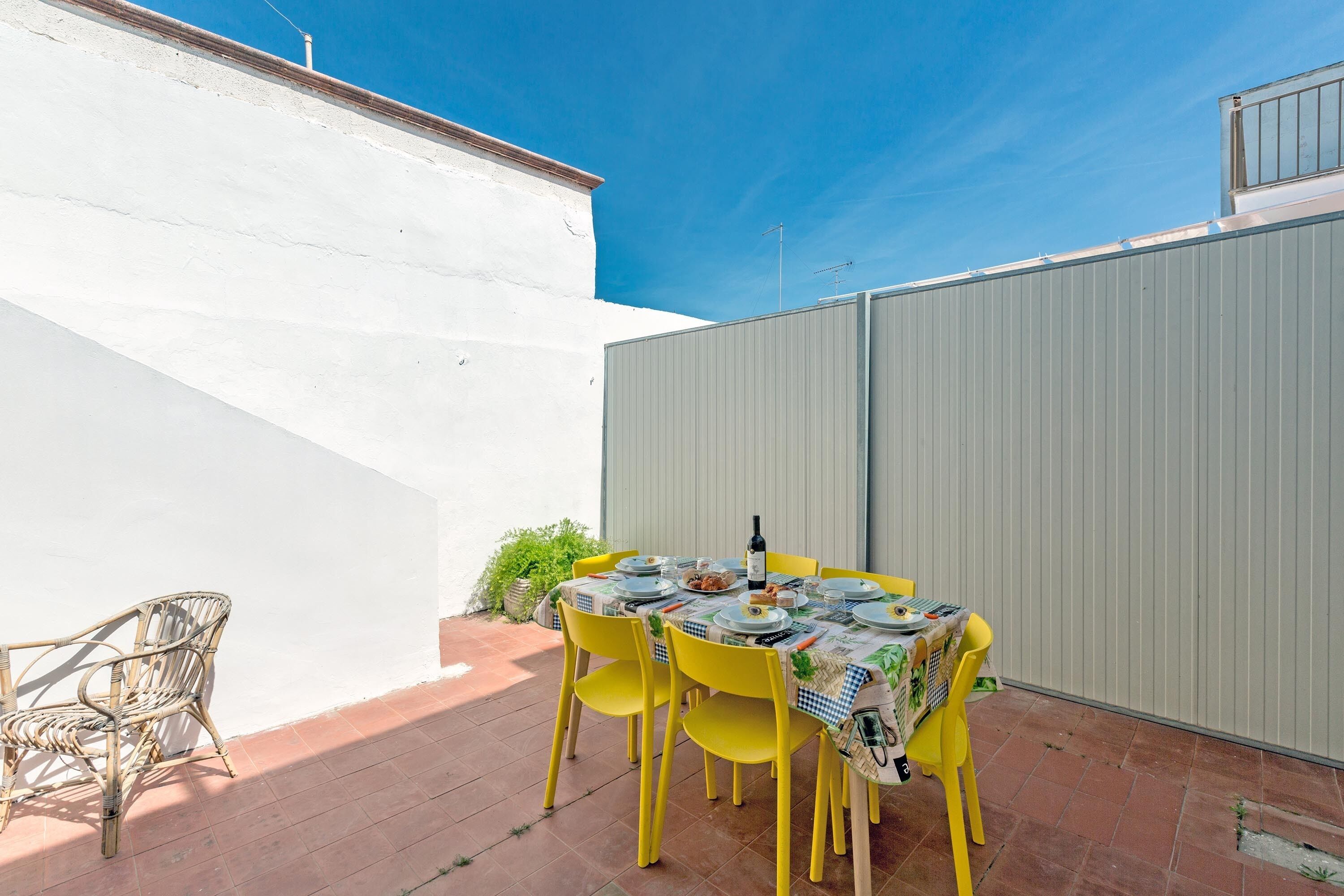 Eine Terrasse mit Esstisch, gelben Stühlen und einem Korbstuhl.