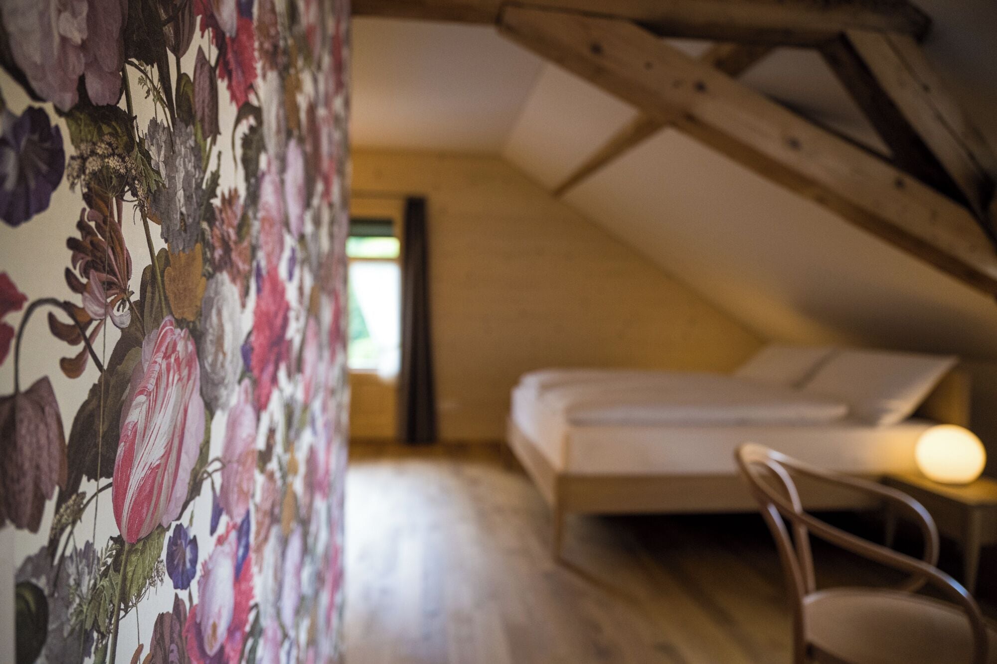 A bedroom with a bed, a chair, and a floral wallpaper.