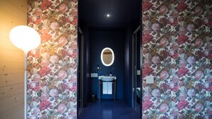 A hallway with floral wallpaper, a round mirror, and a sink with a towel.