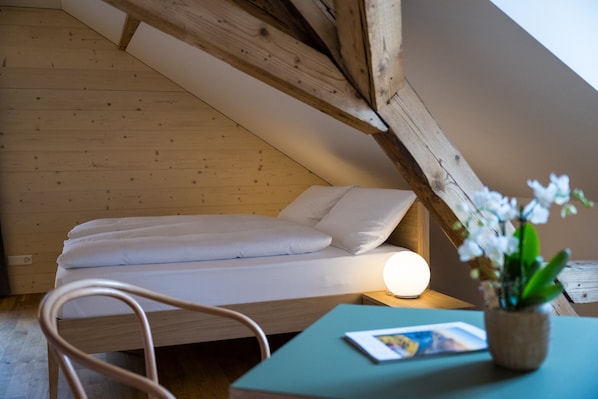 Un dormitorio pequeño y acogedor con una cama individual, una mesita de noche con lámpara y una silla.