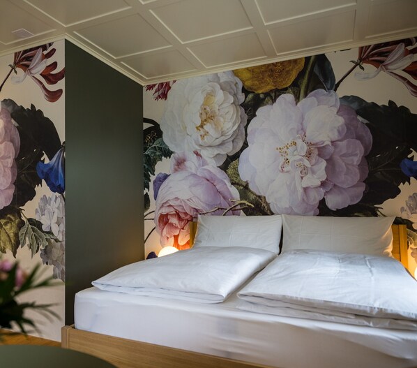 Un dormitorio con cama, papel tapiz floral y una mesita de noche.