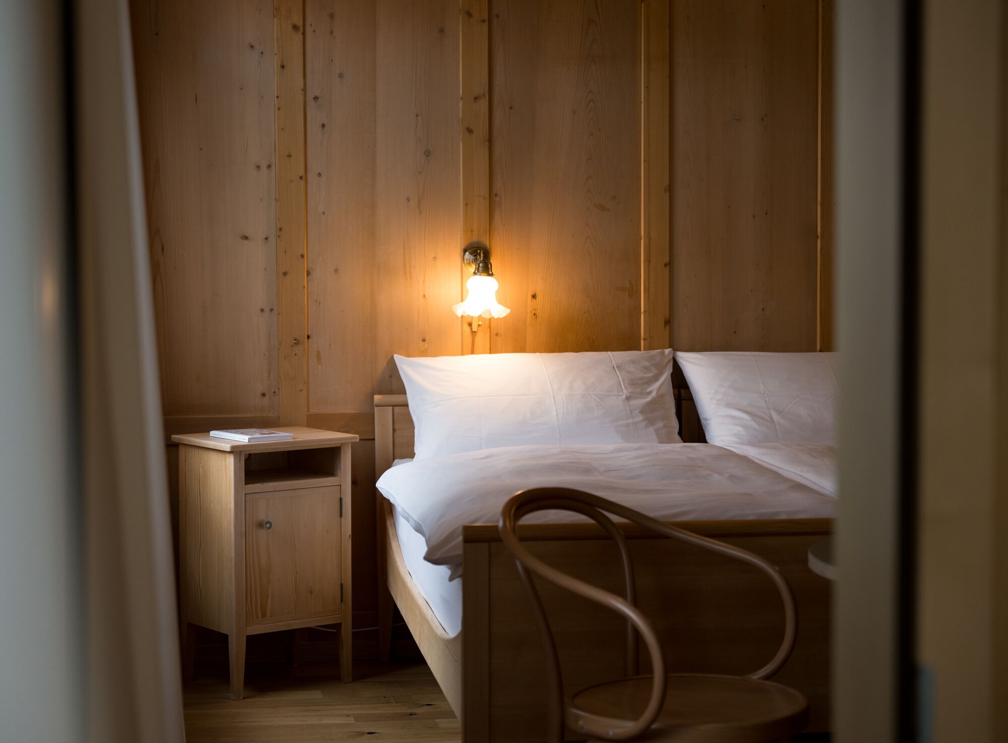 Una habitación con paneles de madera, una cama, una mesita de noche y una silla.