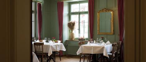 Un comedor con mesas dispuestas para una comida, un espejo grande y una ventana con cortinas.