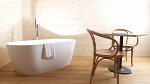 A modern bathroom with a freestanding bathtub, a round wooden table, and a chair.