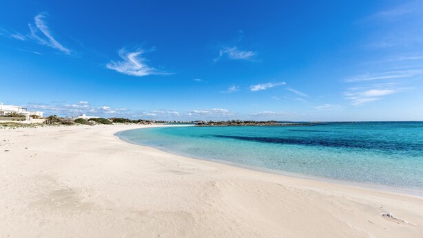 A wide sandy beach with clear turquoise water and a few buildings in the distance. - 3380 Marechiaro - Appartamento C by Barbarhouse (Porto Cesareo)
