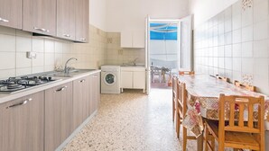 A compact kitchen with a washing machine, a dining area with a table and chairs, and a view through an open door. - 3380 Marechiaro - Appartamento C by Barbarhouse (Porto Cesareo)