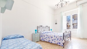 A bedroom with two beds, a nightstand, a window with curtains, and a view of buildings outside. - 3380 Marechiaro - Appartamento C by Barbarhouse (Porto Cesareo)