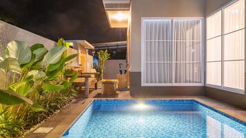 A swimming pool with tiled edges, surrounded by plants and a wooden deck.