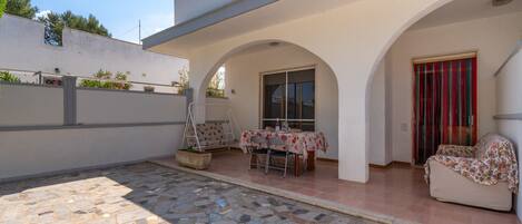 A covered patio area with a stone floor, a table with chairs, and a sofa.