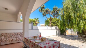 An outdoor patio with a table set for dining, a sofa, and a view of the surrounding garden and buildings. - 3478 Atene - PT By Barbarhouse (Porto Cesareo)