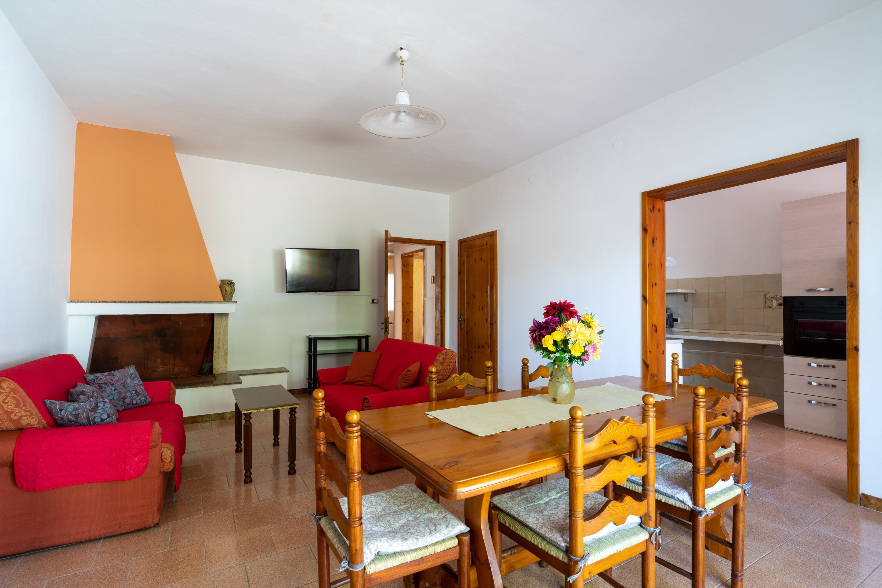 A living room with a wooden dining table, red sofa, and a TV mounted on the wall.