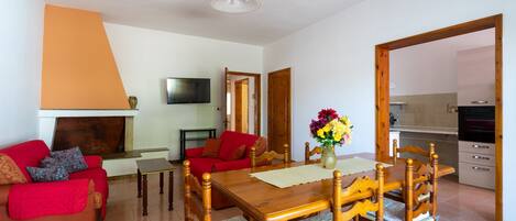 A living room with a wooden dining table, red sofa, and a TV mounted on the wall.