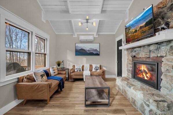 Una sala de estar acogedora con chimenea de piedra, un televisor grande y una zona de estar cómoda con sofá y una mesa de centro.