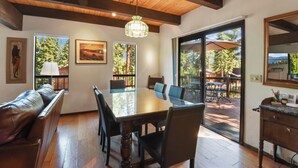 A dining area with a wooden table and chairs, a bench, and a view through glass doors to an outdoor patio.