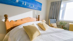 A neatly made bed with a white quilt and two beige pillows, a wooden headboard, and a painting of sailboats on the wall. - Pencoed -  a coastal that sleeps 5 guests  in 3 bedrooms (Llanbedrog)