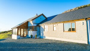 Une maison à deux étages avec un toit en pente, un porche à l’avant et une allée gravillonnée.