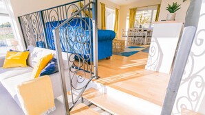 Un salon moderne avec un canapé bleu, des coussins jaunes et un escalier doté d’une rampe en métal décorative.