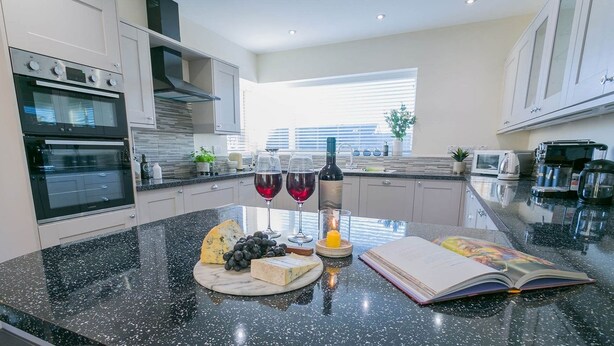 Une cuisine moderne avec un plan de travail en marbre, des verres à vin, une assiette de fromages et un livre.