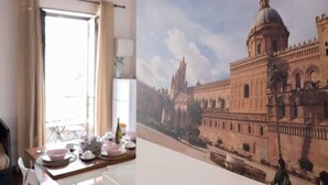 A dining area with a table set for a meal, a window with curtains, and a painting of a historical building.