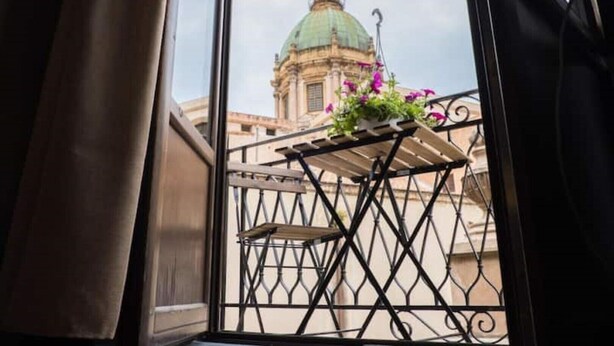 A balcony with a wrought iron railing, a small table, and a hanging plant with purple flowers.