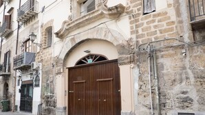 A historic building with a large wooden double door, stone walls, and a small balcony with a metal railing.