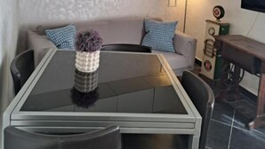 Un salon moderne avec une table à manger au plateau en verre, un canapé agrémenté de coussins à motifs, un meuble fixé au mur et un téléviseur.
