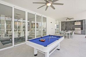 A pool table in a modern room with glass walls, a ceiling fan, and a dining area. - Palmas 15: Luxury villa w/ mosquito net, lap-pool, Jacuzzi, staff & golf cart (Punta Cana)