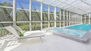 A covered outdoor swimming pool with a glass ceiling, surrounded by white lounge chairs and a view of greenery. - Palmas 15: NEW luxury villa w/ screened-in pool, Jacuzzi, staff & golf cart (Punta Cana)