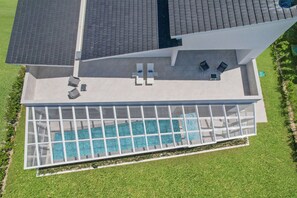 A modern house with a large glass-enclosed swimming pool, a flat roof, and a spacious patio area. - Palmas 15: Luxury villa w/ mosquito net, lap-pool, Jacuzzi, staff & golf cart (Punta Cana)