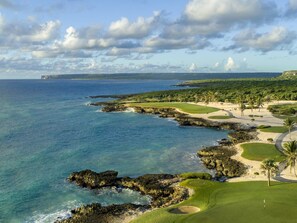 A coastal golf course with a clear view of the ocean, rocky coastline, and a distant mountain range. - Palmas 15: Luxury villa w/ mosquito net, lap-pool, Jacuzzi, staff & golf cart (Punta Cana)