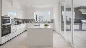 A modern kitchen with a central island, white cabinetry, and a large window. - Palmas 15: NEW luxury villa w/ screened-in pool, Jacuzzi, staff & golf cart (Punta Cana)