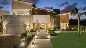 A modern house with a well-lit entrance, a covered patio, and a landscaped garden. - Palmas 15: NEW luxury villa w/ screened-in pool, Jacuzzi, staff & golf cart (Punta Cana)