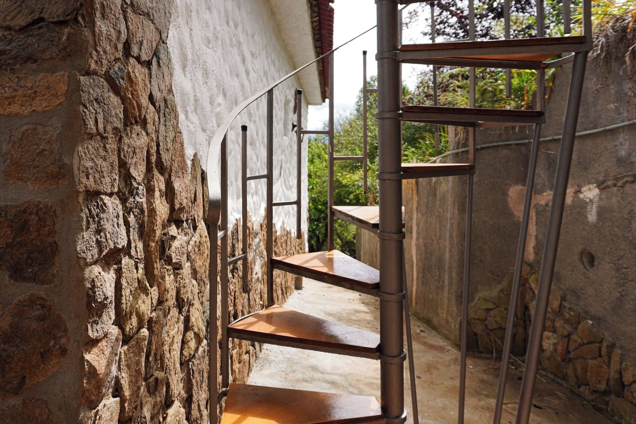 A spiral staircase with metal railings and wooden steps, leading to a stone wall.