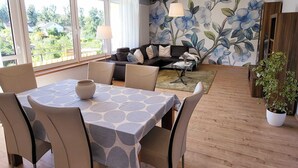 Un comedor con una mesa y sillas, un conjunto de sofás y un mural floral en la pared.