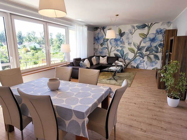 A dining area with a table and chairs, a sofa set, and a floral wall mural.