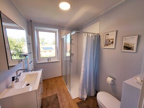 A modern bathroom with a glass shower, a sink, and a toilet. There are two windows providing natural light and a view of the outside.