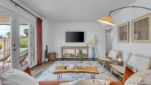 A modern living room with a large TV mounted on the wall, a wooden coffee table, and a seating area with a sofa and chairs. - Sun & Fun, Backyard and Pool (Tempe)
