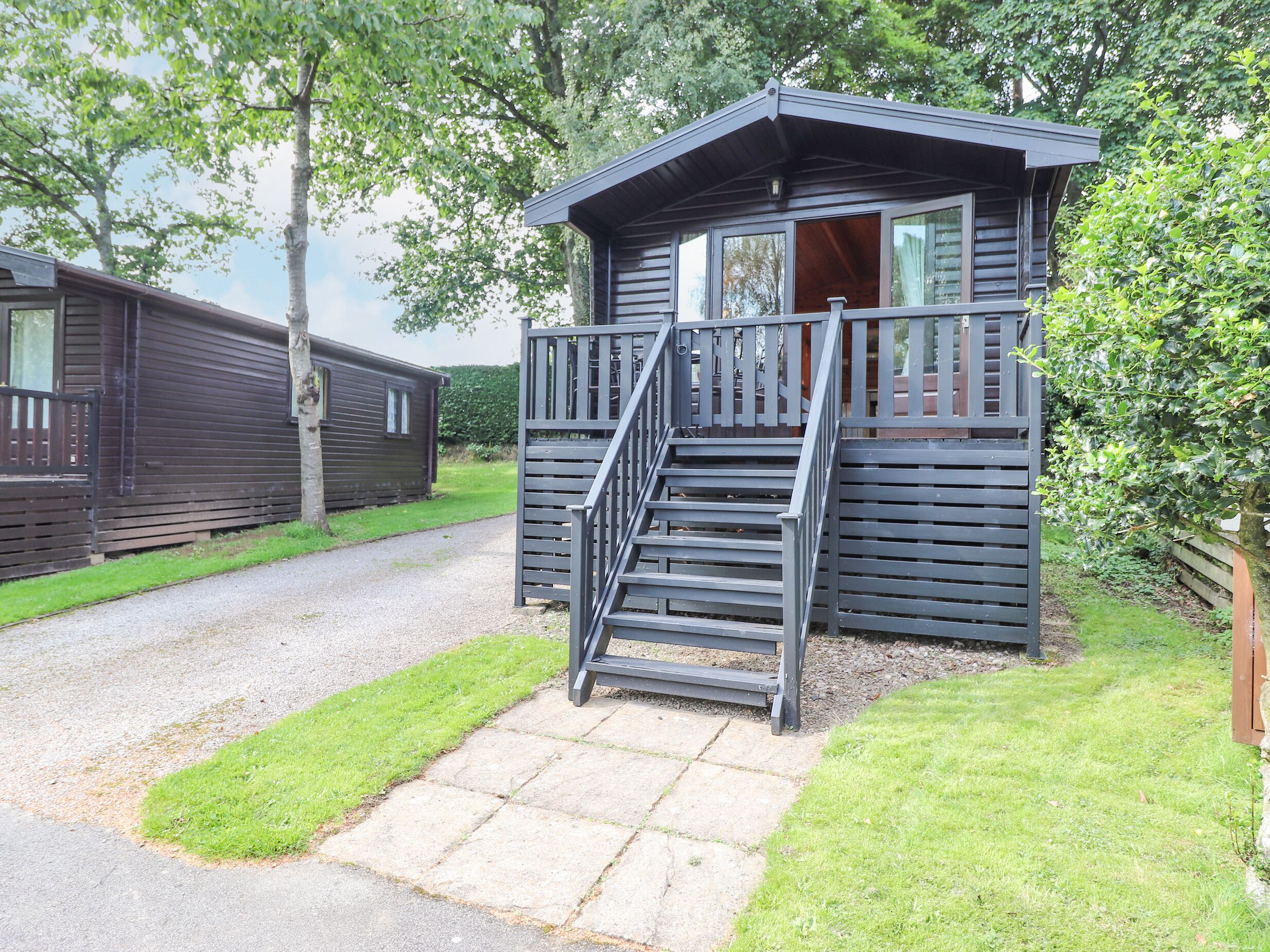 A small, dark-colored cabin with a wooden deck and a set of stairs leading to a door.