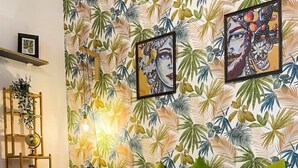 Ein Schlafzimmer mit tropischem Blattmuster-Tapete, einem Bett mit grün-weiß gestrickter Bettwäsche und zwei gerahmten Kunstwerken darüber.