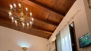 Ein geräumiges Wohnzimmer mit Holzboden, einem grünen Sofa, einem Bett mit grüner Decke, einem Fernseher an der Wand und einem großen Fenster mit Vorhängen.