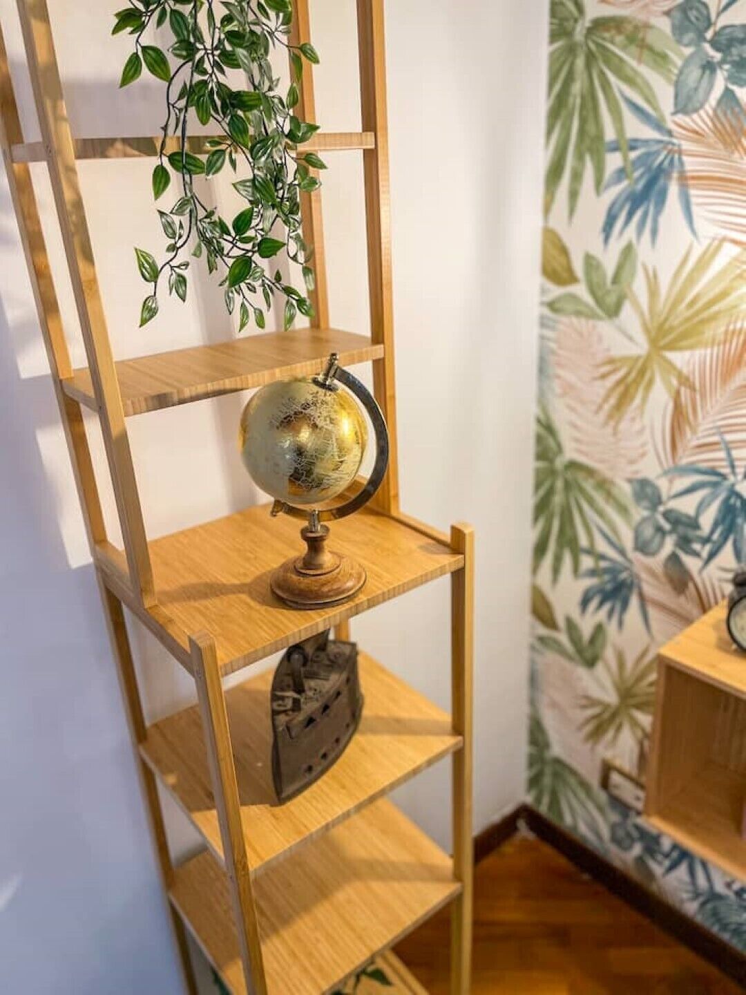 A wooden shelf with a globe and a clock, a hanging plant, and a wall with tropical wallpaper.